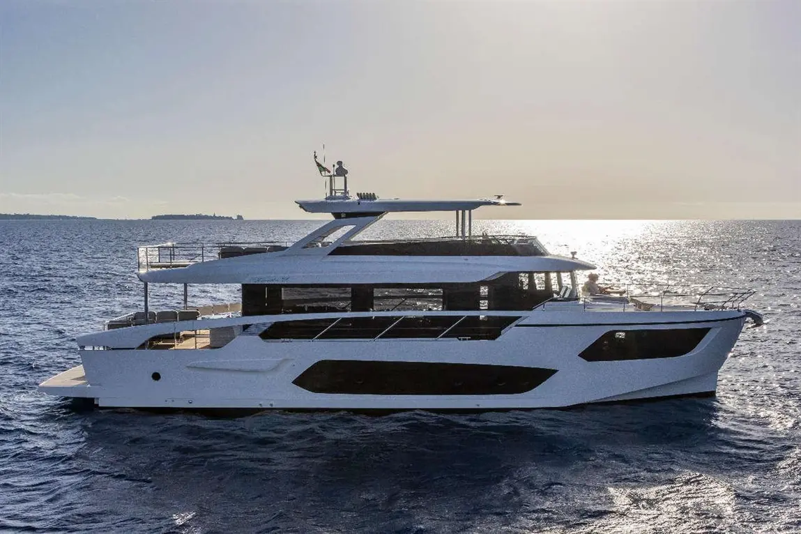 A sleek white luxury yacht sails on the shimmering ocean under a bright sky, with a person at the helm.